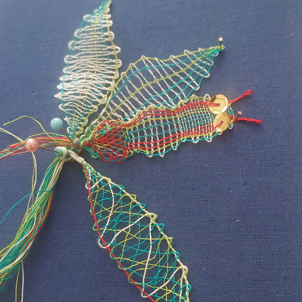 Pequeño insecto y hojas realizados con encaje de bolillos de colores